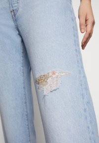 Ljusblå denimjeans med slitna knän som har färgglada broderidetaljer. Jeansen har en rak passform och synlig sömnad.