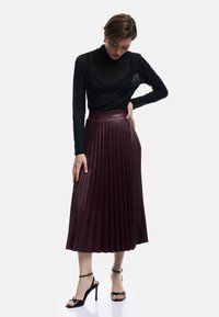Jupe midi plissée bordeaux avec taille haute, associée à un haut noir à manches longues. La jupe présente une texture lisse et des plis bien définis.
