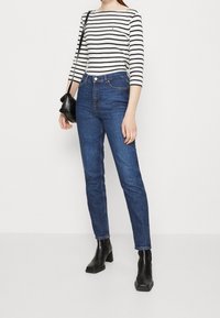 Blå jeans i hög midja med smal passform, kombinerade med en svartvit randig långärmad tröja och svarta stövletter med klack.