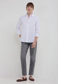 Camicia bianca a maniche lunghe con bottoni, jeans grigi e ballerine nere con stampa leopardata. Tessuto liscio, design aderente, accenti minimi.
