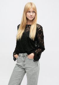 Juodas ilgomis rankovėmis nėriniuotas viršus su gėlių raštu ir varpelio formos rankogaliais, derinamas su pilkomis, aukšto liemens džinsais. Lygus paviršius ir lengvas audinys.