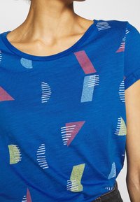 Camiseta azul con patrones geométricos abstractos en rojo, verde y blanco. Escote redondo y mangas cortas con un acabado texturizado.