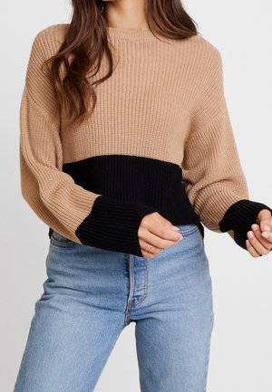 Maglione lavorato a maglia in beige e nero con un design cropped. Presenta maniche lunghe, una texture a coste e ampi polsini neri che contrastano con il corpo.