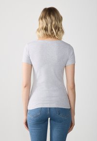 T-shirt gris à manches courtes avec une texture lisse, une coupe ajustée et un col arrondi, associé à un jean bleu.
