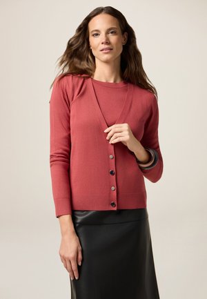 Cardigan in rosa polveroso, scollo a V, polsini a coste, chiusura frontale con cinque bottoni scuri, abbinato a una gonna in pelle nera, texture liscia.