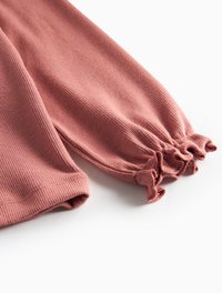 Maglietta a maniche lunghe a coste in rosa tenue con dettagli a volant arricciati ai polsini. Tessuto morbido e design aderente per una vestibilità comoda.