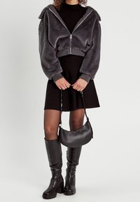 Gray fleece zip-up jacket with bulky sleeves, black fitted turtleneck, black skirt, knee-high black boots, and small black handbag.