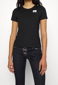 T-shirt di cotone nera con maniche corte e scollo rotondo, caratterizzata da un piccolo logo bianco. Abbinata a jeans di denim scuri.