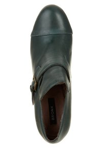 Chaussure à enfiler en cuir vert foncé avec bout arrondi et détail boucle latérale, étiquetée "BRONX" à l'intérieur.