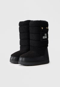 Par de botas de inverno pretas com salto em cunha, com tecido acolchoado, solas de borracha e bolso lateral com botões dourados em forma de coração e o texto "LOVE MOSCHINO".