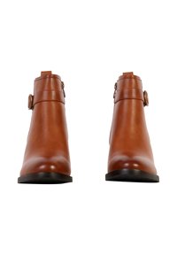 Paire de bottines en cuir marron avec boucles latérales, bouts arrondis et semelles noires, positionnées face avant sur un fond blanc.