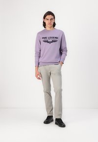 Sudadera de lavanda con texto gráfico negro y diseño de alas, combinada con pantalones gris claro y zapatillas negras. Look sencillo y casual.