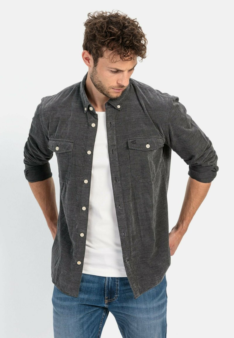Dark gray button-up shirt with chest pockets, long sleeves rolled to the elbows, worn over a white t-shirt and paired with blue jeans.