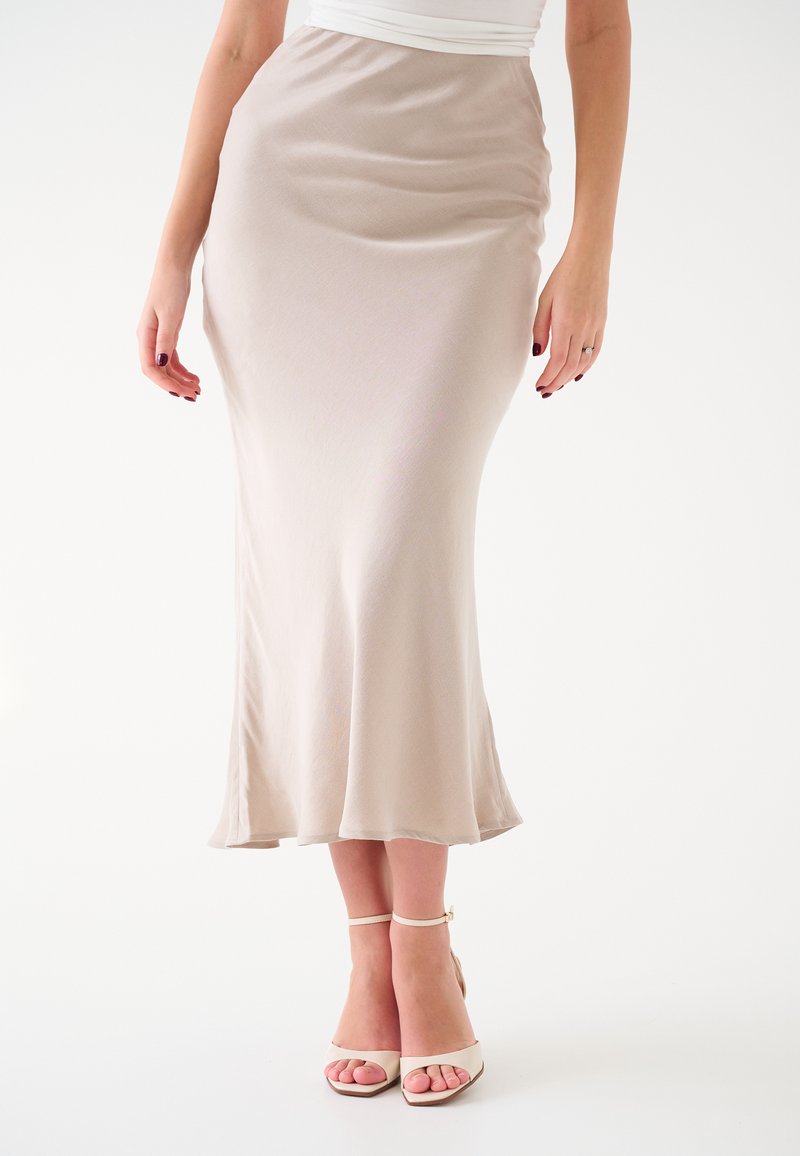 Gonna midi in satin beige chiaro con orlo svasato. Sandali con tacco alto color nude e con cinturini coordinati. Texture liscia e design aderente.