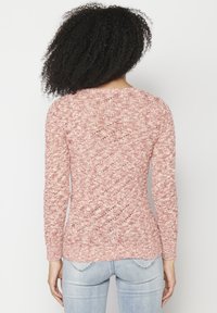 Pull en maille rose clair avec manches longues, motif texturé et encolure arrondie. Vue de dos montrant une silhouette ajustée et des poignets côtelés.