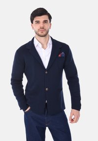 Cardigan lavorato a maglia blu navy con colletto a revers, due tasche frontali, chiusura con un singolo bottone marrone e un fazzoletto da taschino a fantasia.