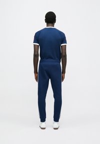 Tumszils sporta tērps ar īsām piedurknēm un baltām detaļām, kā arī atbilstošas bikses ar sānu svītrām, izgatavots no mīksta auduma.