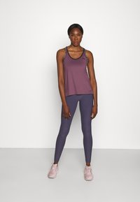 Lila sporttop med svarta detaljer och axelband; matchad med strukturerade, mörklila leggings och ljusrosa löparskor.