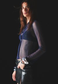 Marinblus i transparent material med silvertrådar, lång ärm och knappslå framtill, kombinerat med en läderkjol och metallarmband.