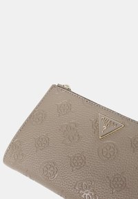 Portafoglio marrone con texture, con motivi in rilievo, accento a logo triangolare e chiusura con zip. Presenta una leggera lucentezza e bordi cuciti.