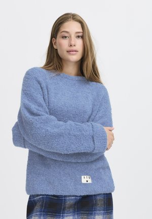 Blue, textured sweater with long sleeves and a crew neckline. Features a small tag with "STD" and a heart at the hem.