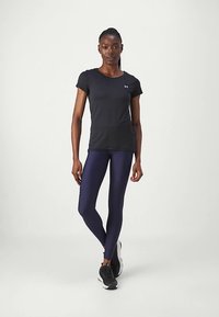 Fekete, rövid ujjú sportfelső sötétkék leggingssel párosítva. Az anyag simának, rugalmasnak és légáteresztőnek tűnik, aktív viselethez ideális.