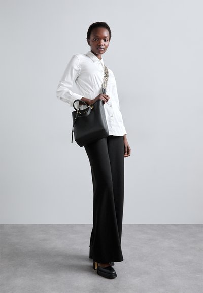 Borse nera con accenti dorati, camicia bianca a maniche lunghe, pantaloni neri a gamba larga e scarpe nere. Texture lisce, design strutturato.