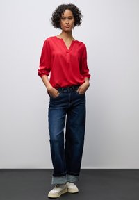 Červená volná blůza s výstřihem do V a tříčtvrtečními rukávy, ve spojení s tmavě modrými širokými džínami a bílými teniskami.