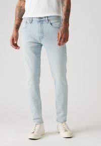 Lys blå denimjeans med slim fit, som har fem lommer, glidelås og subtile sømdetaljer. Kombinert med hvite høye sneakers.