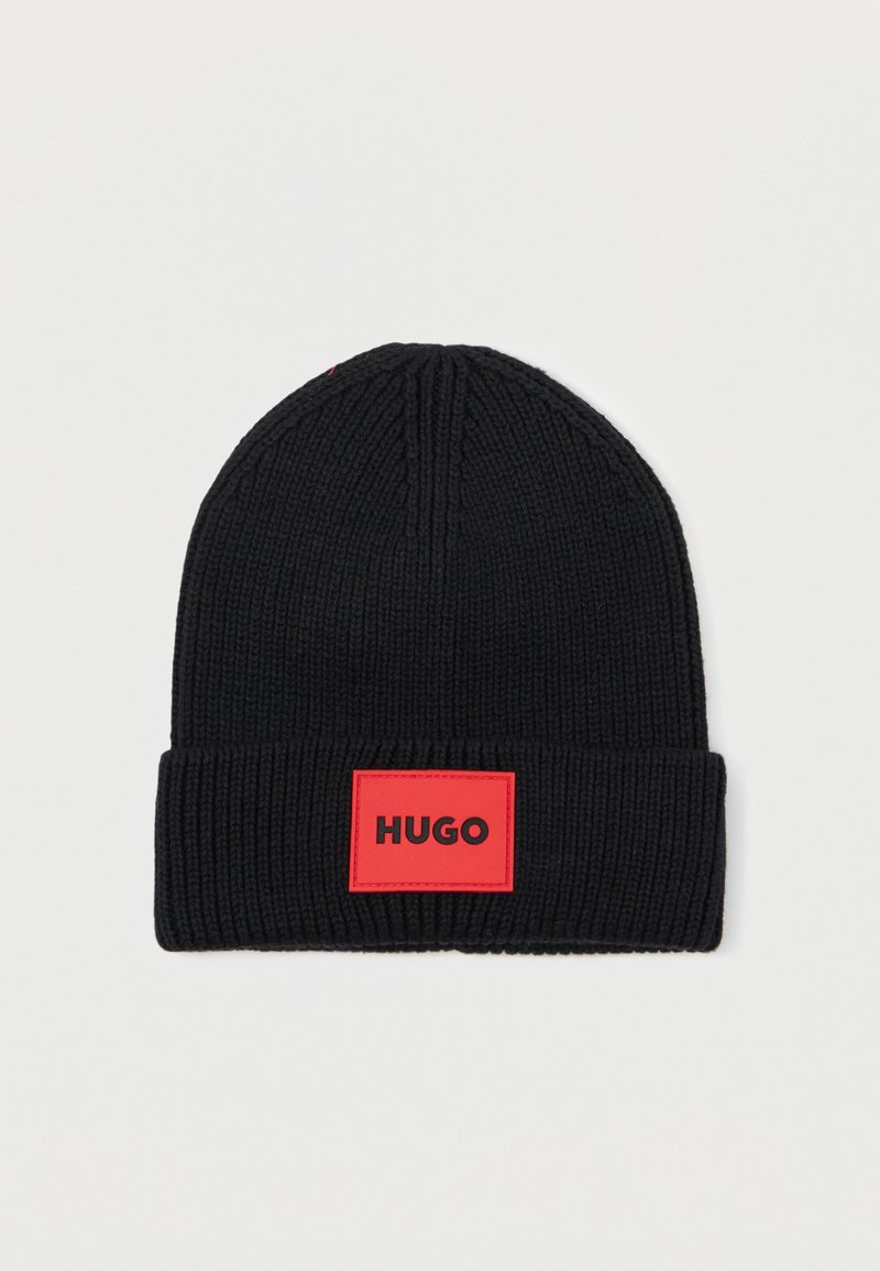 Berretto in maglia nera con texture a coste e risvolto. Presenta un'etichetta rettangolare rossa con la scritta "HUGO" in lettere nere.