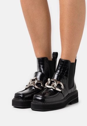 Mustat nilkkurit, joiden pinta on krokotiilinihkopainettua, hopeaketjusomiste, joustavat sivupaneelit ja paksu, teksturoitu pohja.