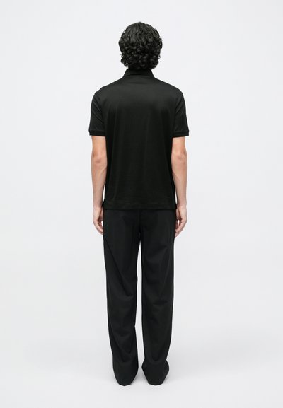 Juoda polo marškinėliai trumpomis rankovėmis, lygios tekstūros. Derinami su juodomis kelnėmis, abu pasiūti pagal figūrą. Paprastas dizainas, be matomų raštų.