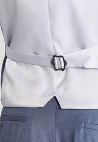 Tela blanca en la parte posterior con un acabado texturizado, presenta una correa horizontal asegurada con una hebilla de metal plateada, unida a una tela azul texturizada.