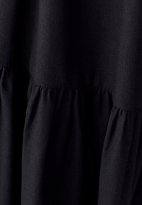 Juodas suknelė, pagaminta iš tekstūruotos medžiagos, su sluoksniuotu dizainu ir raukšlėtės akcentais juosmens linijoje, rodanti glotnų ir tolygų apdailą.