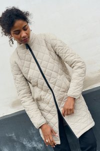 Beige kviltet jakke med høj krave og lynlås. Har et diamantmønster, elastiske manchetter og en lige skæring.