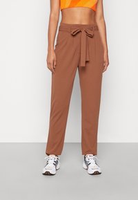 Bruine, hoogsluitende broek met een strikceintuur in de taille, met een recht model dat licht valt. De textuur is glad.