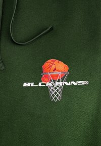 Groene hoodie met een basketbalafbeelding in oranje en wit, met de tekst "BLCKBNNS" onder het ontwerp, gemaakt van zachte stof.