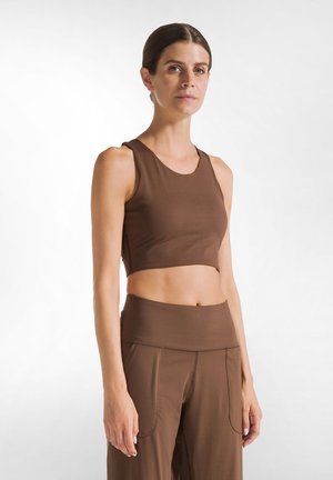 Brun kortärmad crop top i elastisk tyg, med rund halsringning och breda axelremmar, tillsammans med högmidjade bruna byxor.