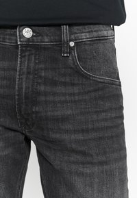 Jeans de denim cinza escuro com um design clássico de cinco bolsos, uma textura horizontal subtil e um botão metálico da marca Lee.