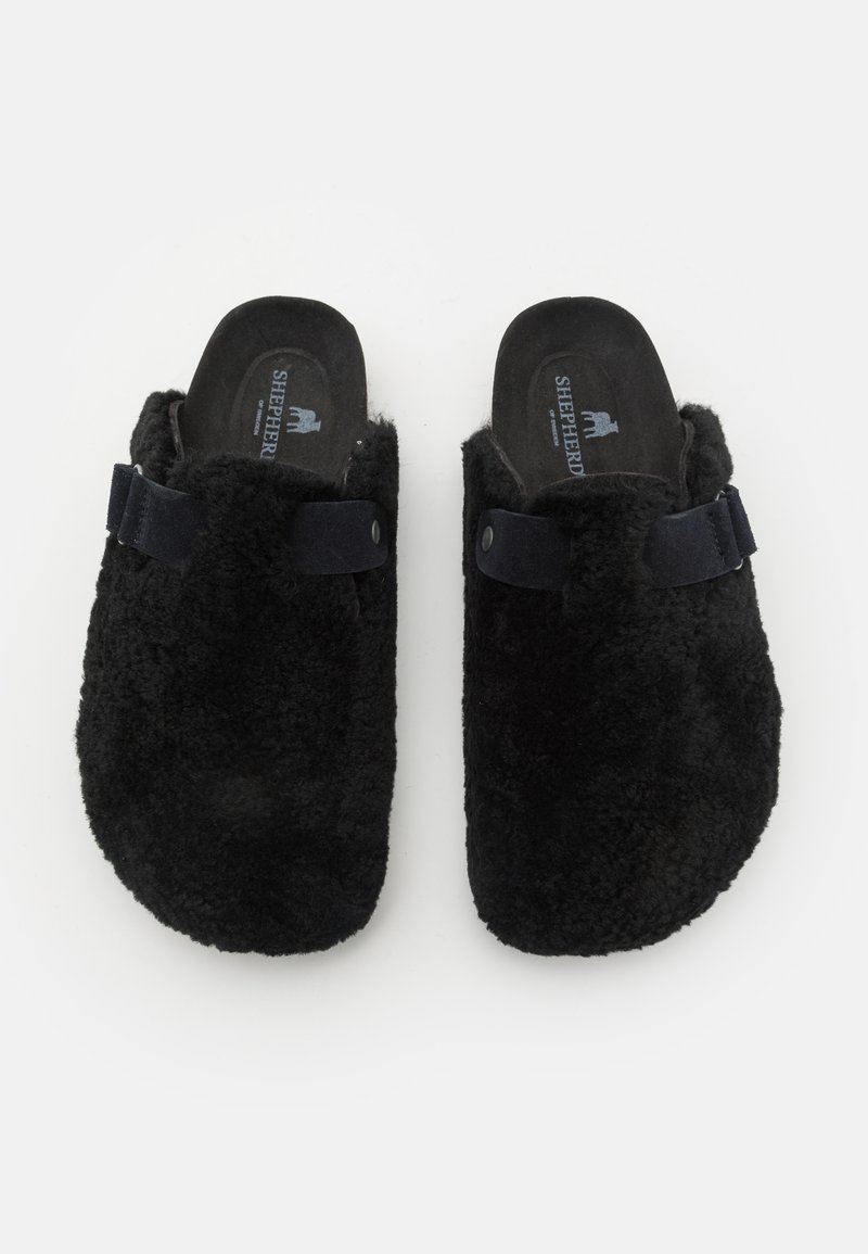 Schwarze, flauschige Hausschuhe mit einer weichen Textur, runder Form und einem Stoffriemen oben. Rutschdesign mit einer gepolsterten Innensohle.