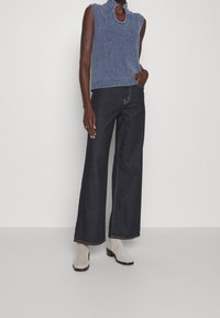 Top sin mangas de punto azul con cuello alto, combinado con vaqueros de pierna ancha de mezclilla oscura y botas de tobillo gris claro. Diseño casual en un color sólido.
