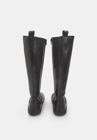 Mustad mustad kuni põlvedeni ulatuvad nahksaapad, millel on sile tekstuur, tõmblukuga sulgemine ja elastsed külgpanelid mugavuse tagamiseks. Tasased taldad ja minimaalne disain.