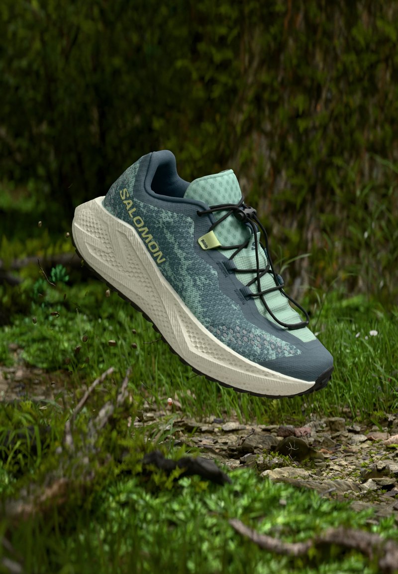 Πράσινο και σκούρο μπλε παπούτσι για τρέξιμο με υφασμάτινο επάνω μέρος με υφή, σύστημα κορδονιών και ευλύγιστο πάτο. Διακριτικό λογότυπο Salomon στο πλάι.