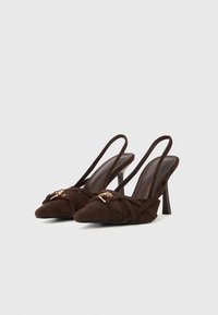 Rjave semiš čevlji z visoko peto in odprto peto, z ostrimi konicami, prepletenimi trakovi in zlatimi okrasnimi elementi. Gladko notranjo podlogo in vitke pete.