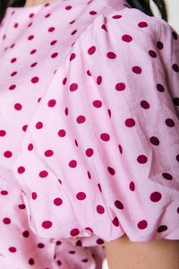 Ροζ μπλούζα με μεγάλα μπορντό πουά, με φουσκωτά μανίκια και υφή υφάσματος. Κοντινή λήψη που τονίζει το μοτίβο και το σχέδιο των μανικιών.