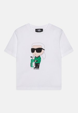 Maglietta bianca in cotone con un grafico a cartone animato di un personaggio con occhiali da sole e un maglione verde a fantasia che tiene un microfono e un accessorio.