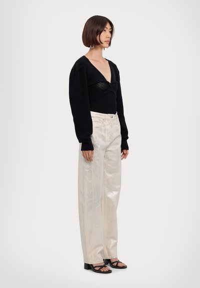 Maglione nero a maniche lunghe, vita aderente; pantaloni bianchi lucidi a gamba larga; sandali neri con tacco a blocco e dettagli in fascia.