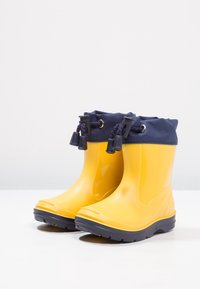 Žluté gumové dešťové boty s námořnickým textilním lemováním, vybavené stahovací šňůrkou a texturedními podrážkami pro lepší přilnavost.