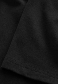 Zwarte katoenen t-shirtstof, gladde textuur, heeft een gestikte zoom en een licht verfrommelde uitstraling. Zachte val zonder zichtbare patronen.