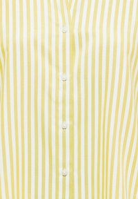 Tissu rayé verticalement jaune et blanc avec des boutons blancs cousus en ligne verticale au centre.